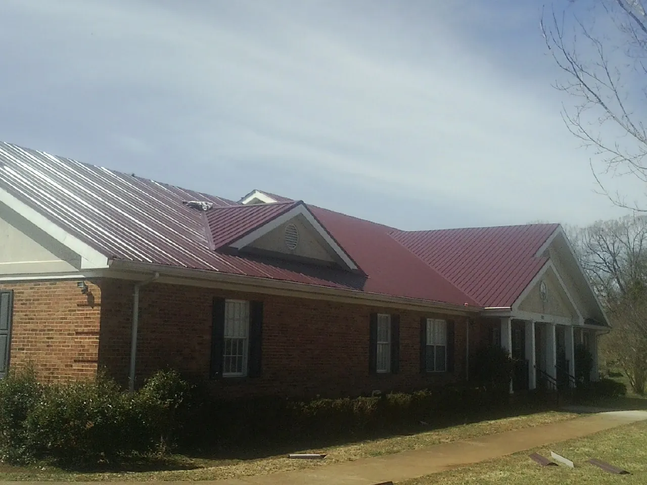 Red metal roof with gabled entries on a long brick building, from a Hail Damage Roof Repair job in Shelby